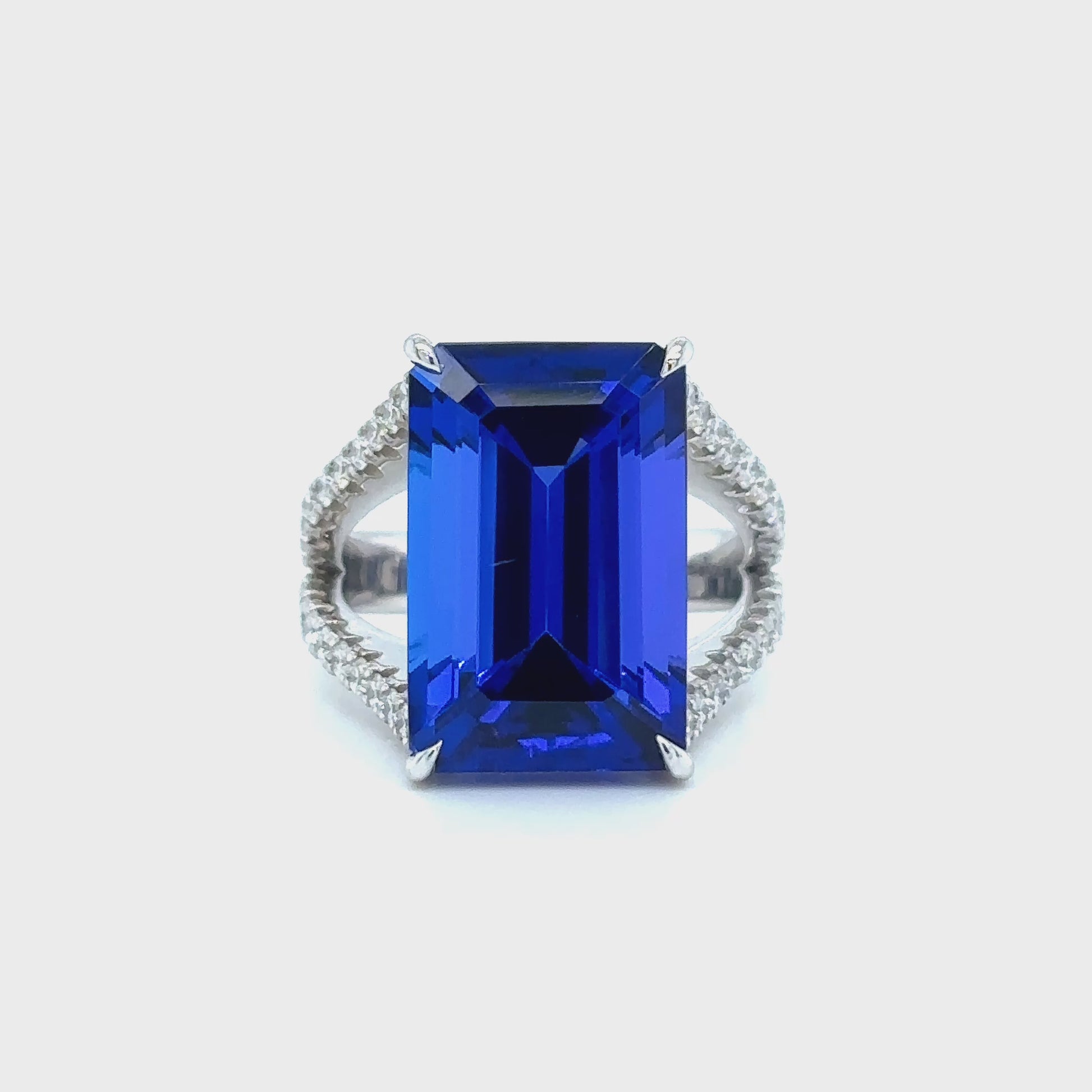 Emerald cut tanzanite ring with split shank diamond band, Elegant emerald cut tanzanite and diamond ring with split shank design, Split shank ring featuring vibrant emerald cut tanzanite center stone, White gold ring with emerald cut tanzanite and diamond accents, Luxurious emerald cut tanzanite ring framed by split shank diamonds, Statement ring with emerald cut tanzanite and diamond split shank, Modern split shank diamond ring with vivid emerald cut tanzanite