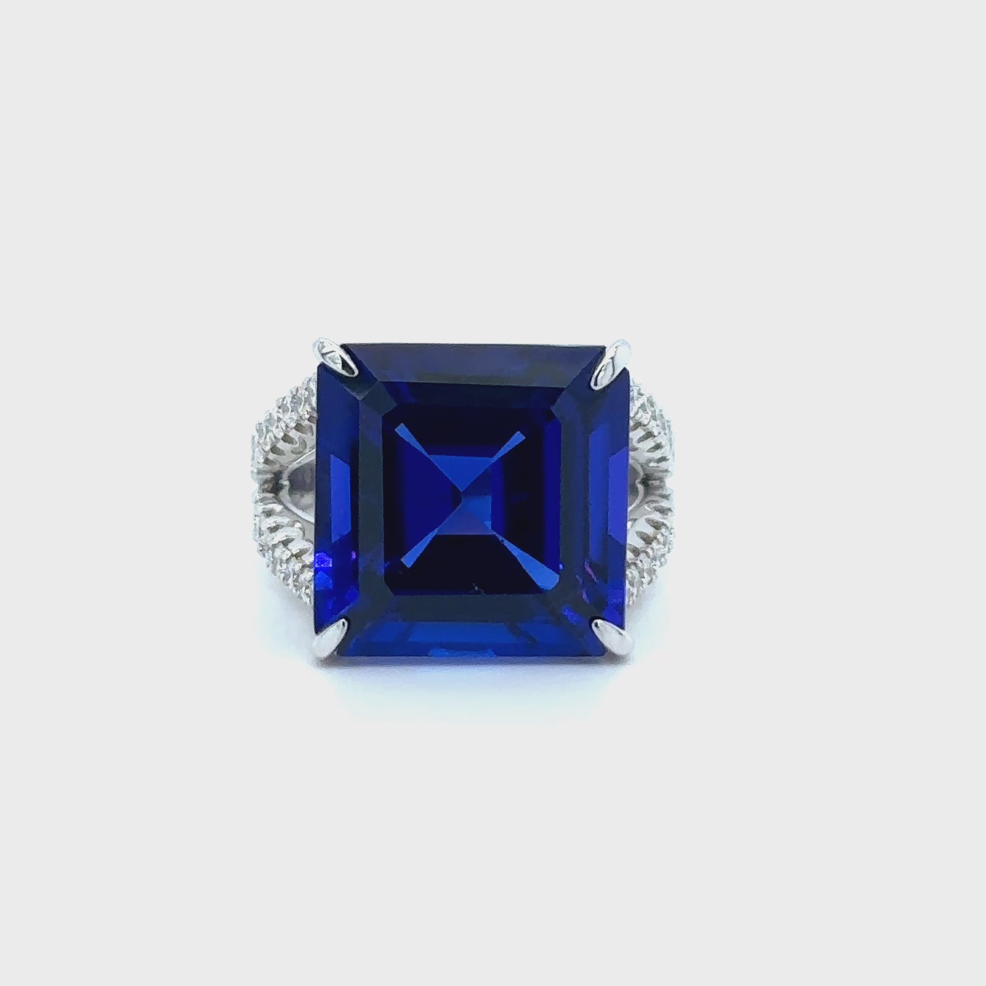 Square emerald-cut tanzanite ring with split shank diamond band, Elegant split shank ring featuring square emerald tanzanite center stone, Luxury tanzanite and diamond ring with emerald-cut design, White gold ring with square emerald tanzanite and split shank detail, Bold emerald-cut tanzanite ring with sparkling diamond split band, Square tanzanite gemstone ring with modern split shank setting, Sophisticated split shank diamond ring with emerald-cut tanzanite centerpiece