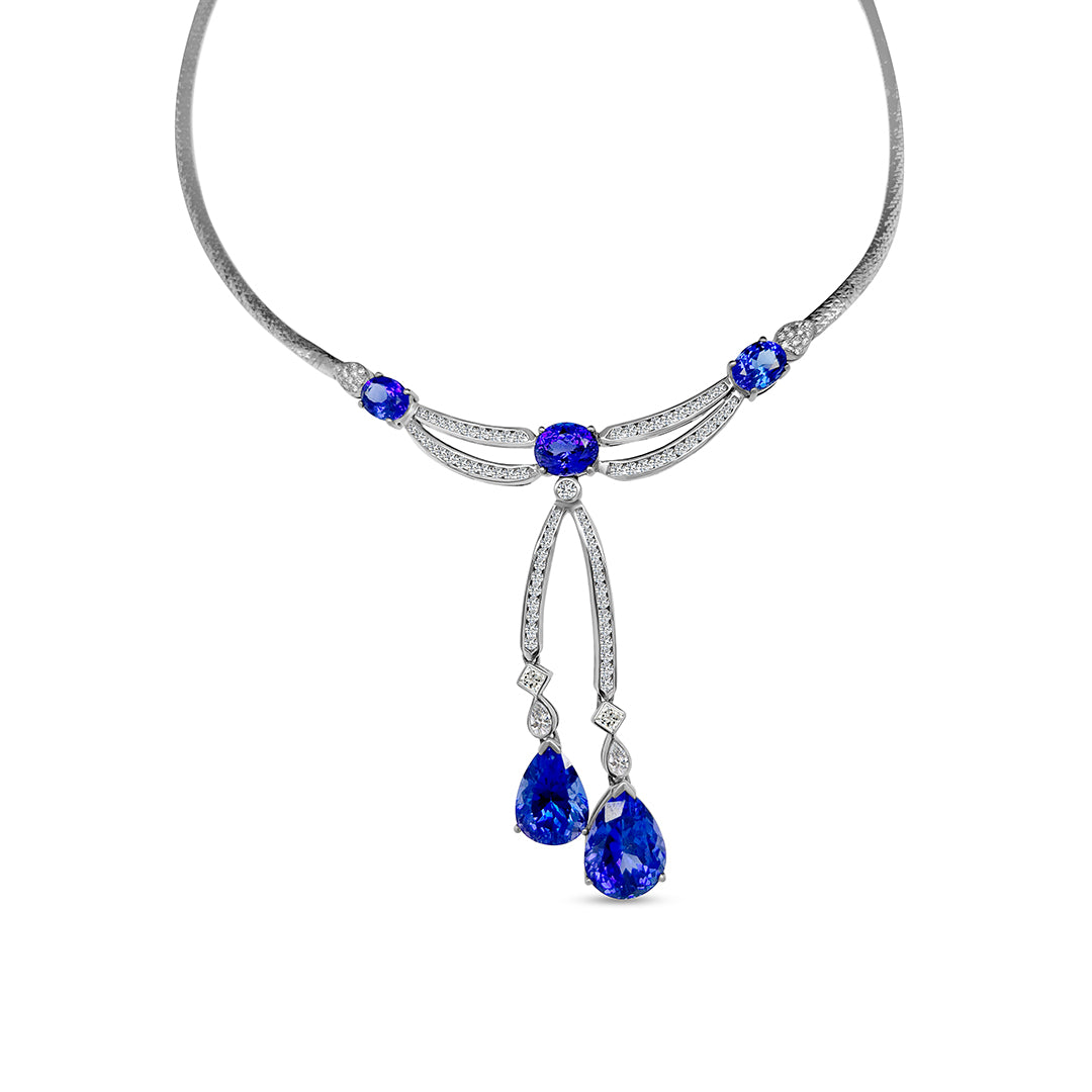 Main Image: "16.70ct Oval & Pear Shaped Tanzanite & Diamond Pendant" Tanzanite Detail: "Oval and Pear Shaped Tanzanite Gems" Diamond Halo: "Diamond Halo Accentuating Tanzanite Pendant" Pendant Profile: "Luxurious Design with Interchangeable Liners" Customizable Liners: "Different Open Liner Options for Personalization" Elegance in Motion: "Tanzanite and Diamond Pendant Capturing Movement"