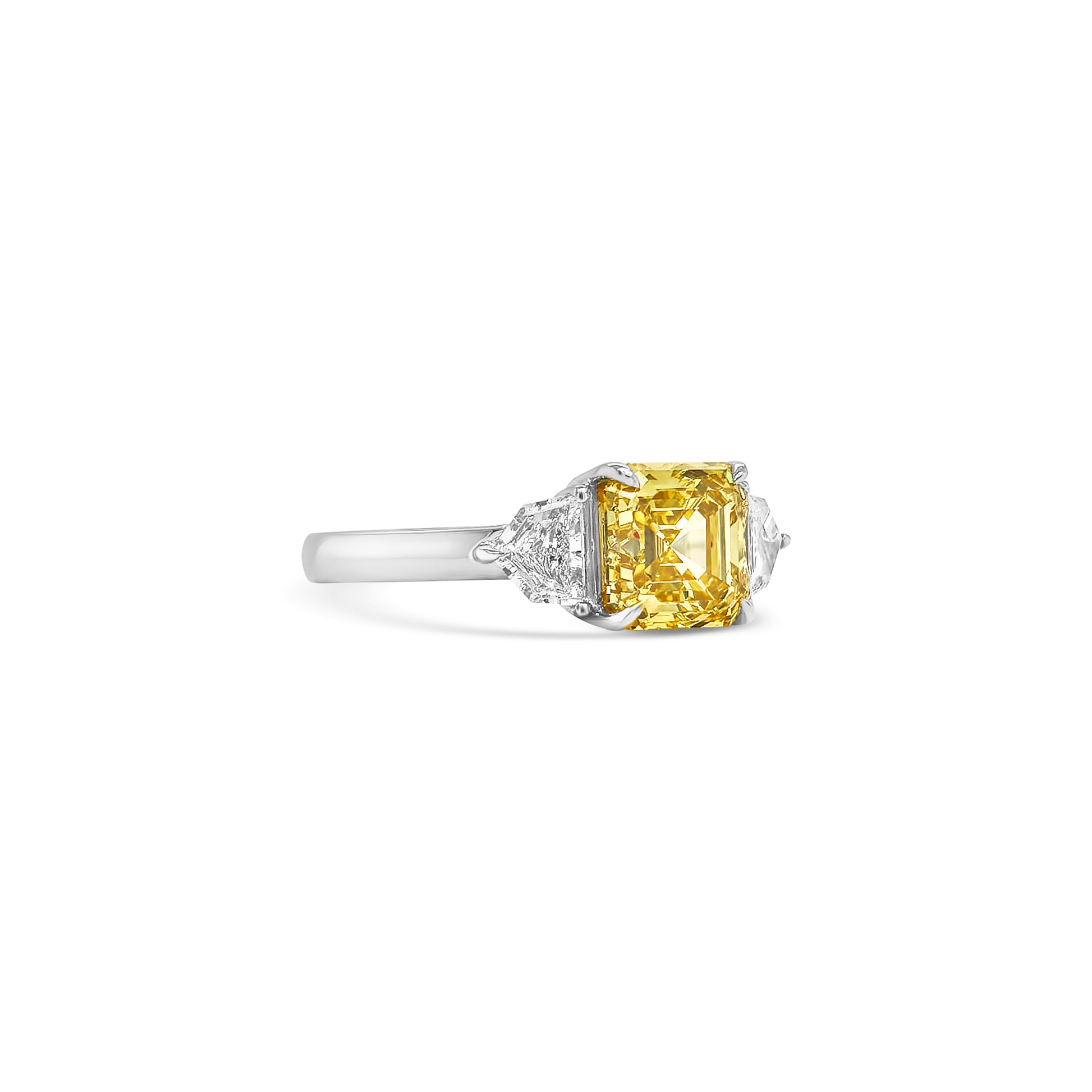 Discover the timeless elegance of this Fancy Yellow Square Emerald Diamond Trilogy Ring, featuring an exquisite yellow emerald-cut diamond and dazzling Cadillac side stones.