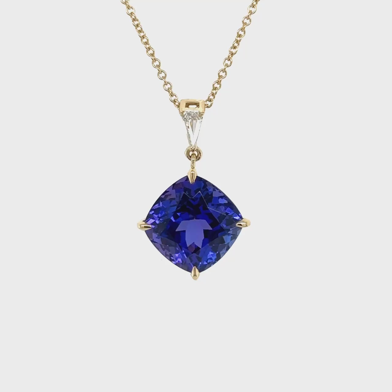 A cushion cut tanzanite pendant, sparkling with diamonds, radiant gemstone jewelry, luxurious tanzanite necklace, dazzling diamond and tanzanite pendant, elegant gemstone pendant, exquisite cushion cut tanzanite and diamond necklace.