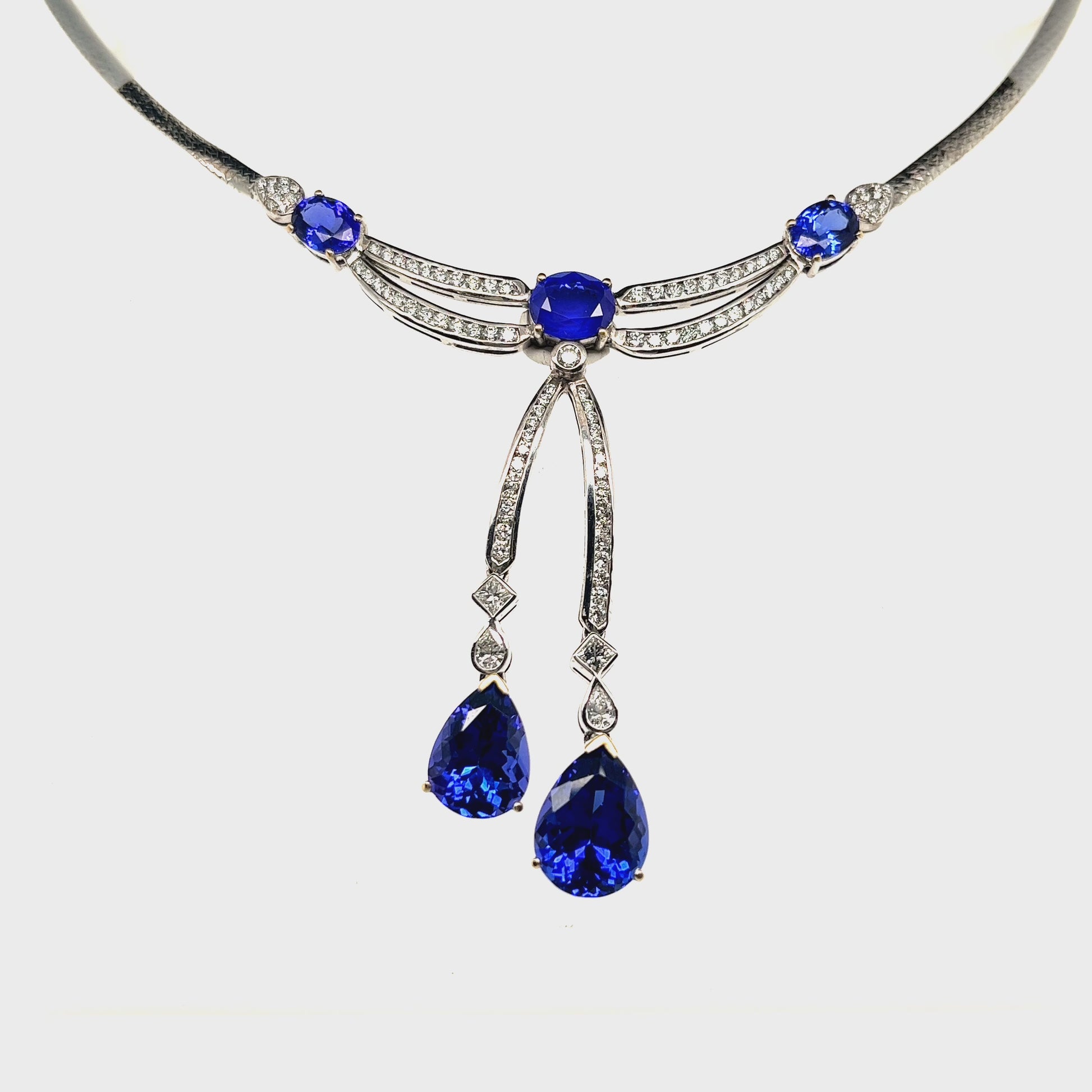 Main Image: "16.70ct Oval & Pear Shaped Tanzanite & Diamond Pendant" Tanzanite Detail: "Oval and Pear Shaped Tanzanite Gems" Diamond Halo: "Diamond Halo Accentuating Tanzanite Pendant" Pendant Profile: "Luxurious Design with Interchangeable Liners" Customizable Liners: "Different Open Liner Options for Personalization" Elegance in Motion: "Tanzanite and Diamond Pendant Capturing Movement"
