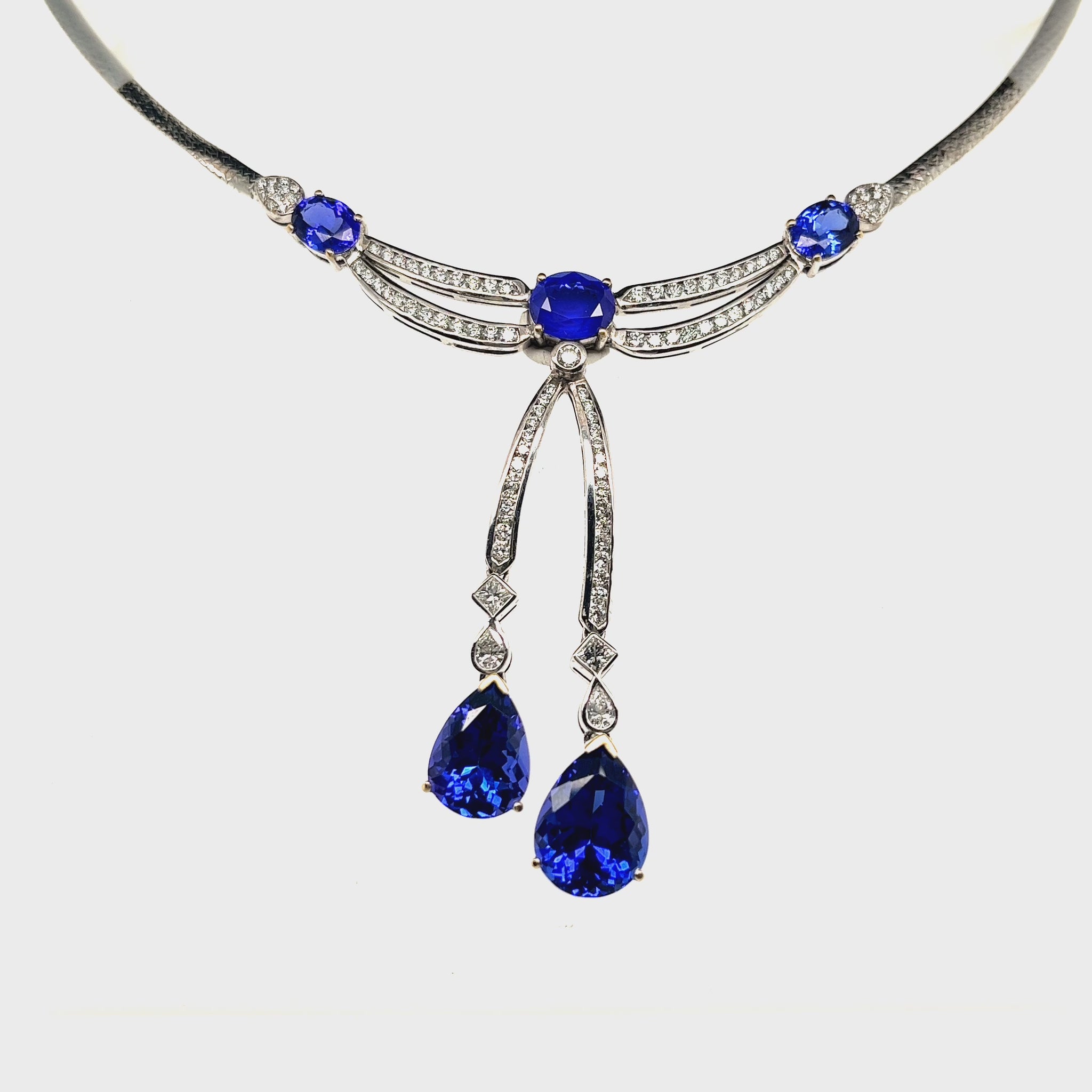 Main Image: "16.70ct Oval & Pear Shaped Tanzanite & Diamond Pendant" Tanzanite Detail: "Oval and Pear Shaped Tanzanite Gems" Diamond Halo: "Diamond Halo Accentuating Tanzanite Pendant" Pendant Profile: "Luxurious Design with Interchangeable Liners" Customizable Liners: "Different Open Liner Options for Personalization" Elegance in Motion: "Tanzanite and Diamond Pendant Capturing Movement"